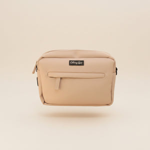 A beige nylon pouch bag with a black brand label reading 'Odezy Gear' sitting on a brown fabric armchair.