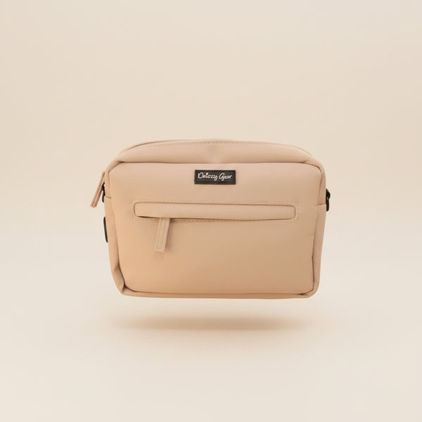 A beige nylon pouch bag with a black brand label reading 'Odezy Gear' sitting on a brown fabric armchair.