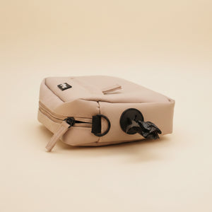 A cream-colored leather zippered pouch or small bag with black hardware, shown resting on a brown textured surface against a matching brown background.
