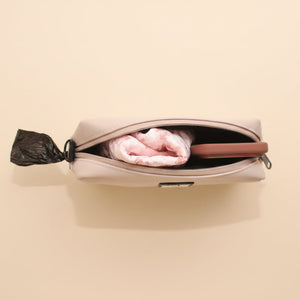 A beige zippered pouch or small bag shown from above, partially unzipped to reveal a pink folded item inside, set against a brown textured background.