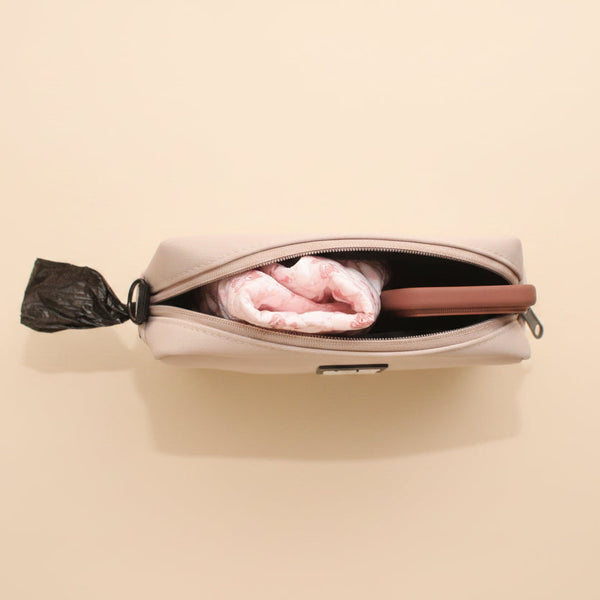 A beige zippered pouch or small bag shown from above, partially unzipped to reveal a pink folded item inside, set against a brown textured background.