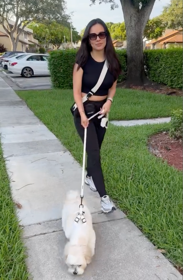 Woman walking a white dog on a leash in a suburban neighborhood