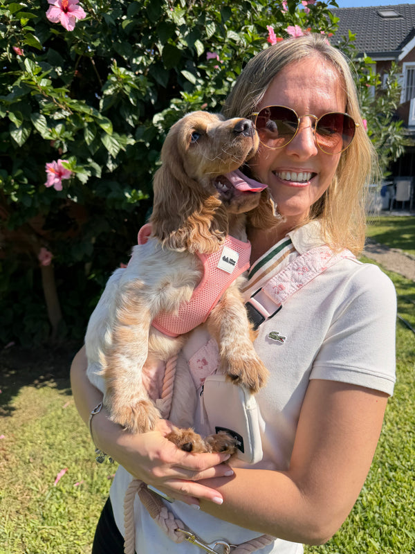 Woman holding a small dog in a park with greenery and flowers in the background
