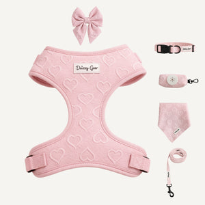 Pink pet harness with heart patterns, matching collar, leash, and bandana on a white background.