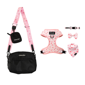 A pet accessory set from Colby Girl, featuring a black crossbody bag with a pink patterned strap, a matching pink heart-patterned harness, collar, bow tie, and bandana, displayed on a clean white background.
